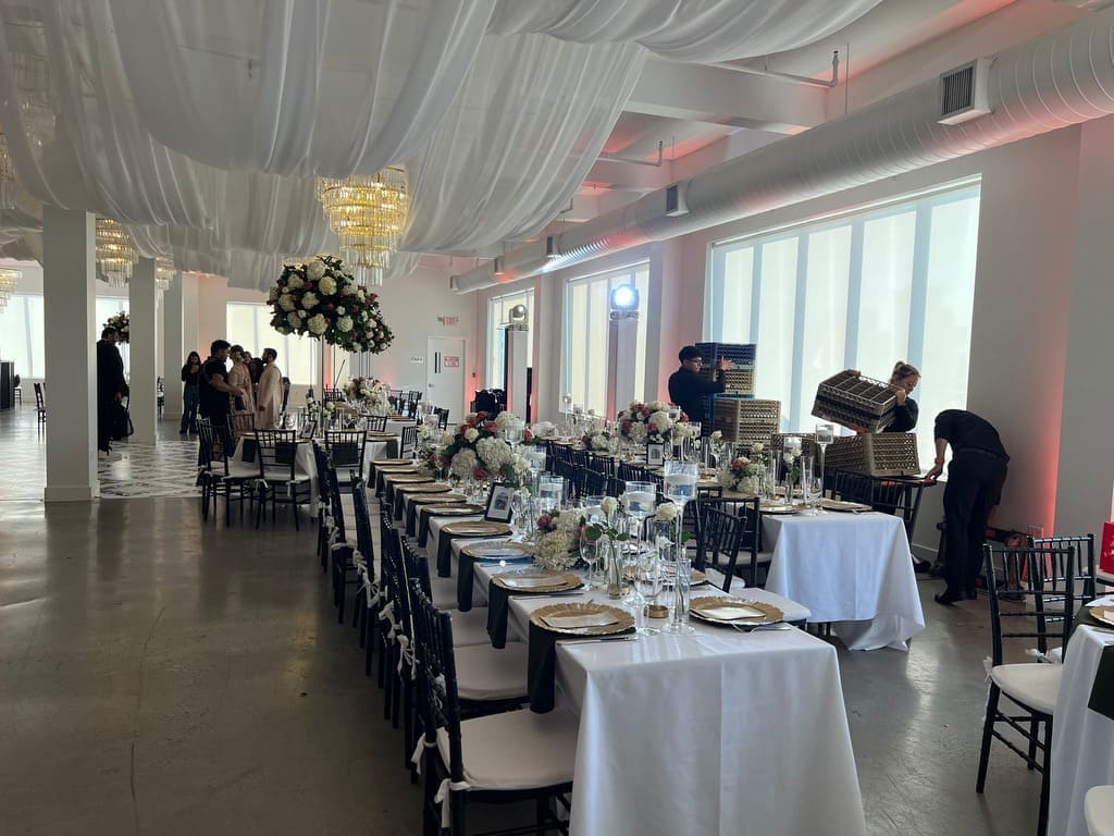 Elegant wedding reception setup with floral centerpieces, decorated tables, and event staff preparing the venue for guests.