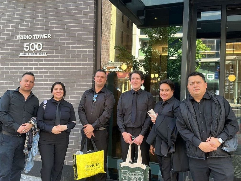 Group of event staff dressed in professional black attire standing outside a modern building, ready for corporate or private event assistance.